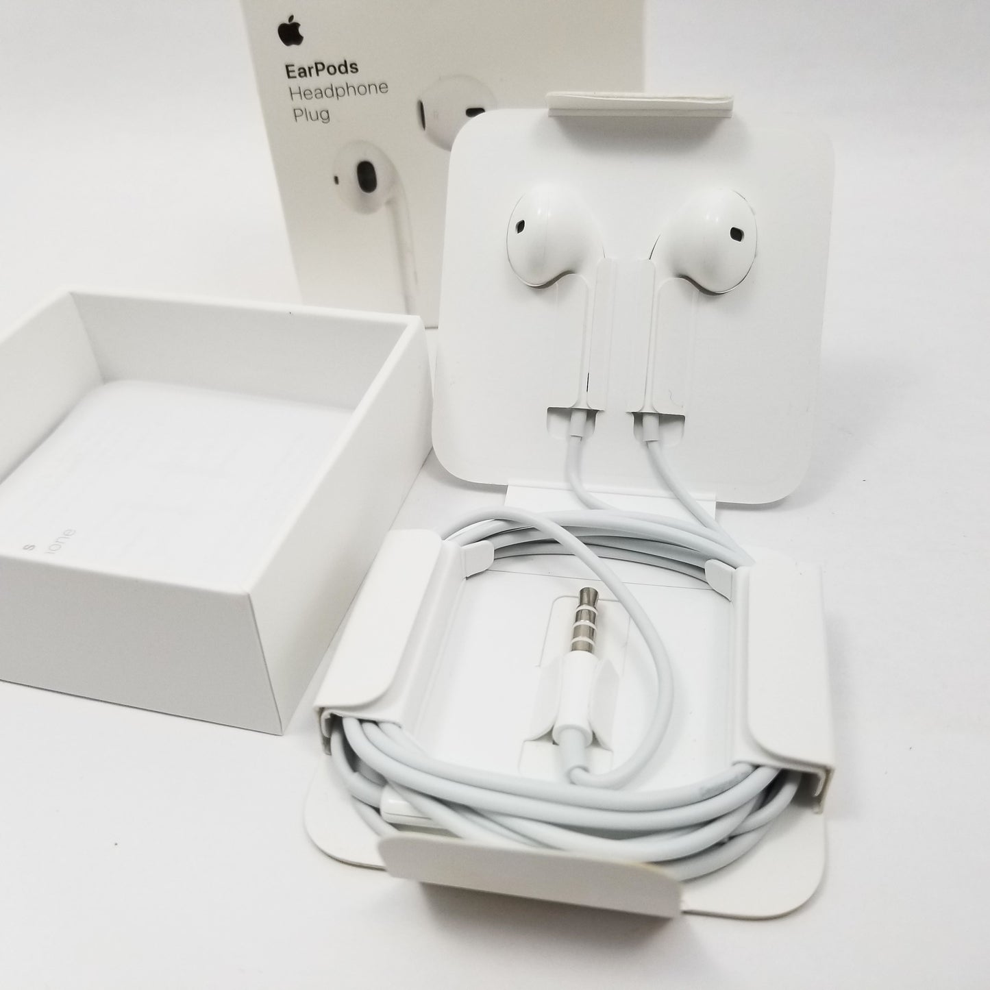 Apple earpods wound up in retail packaging with retail packaging in the background.