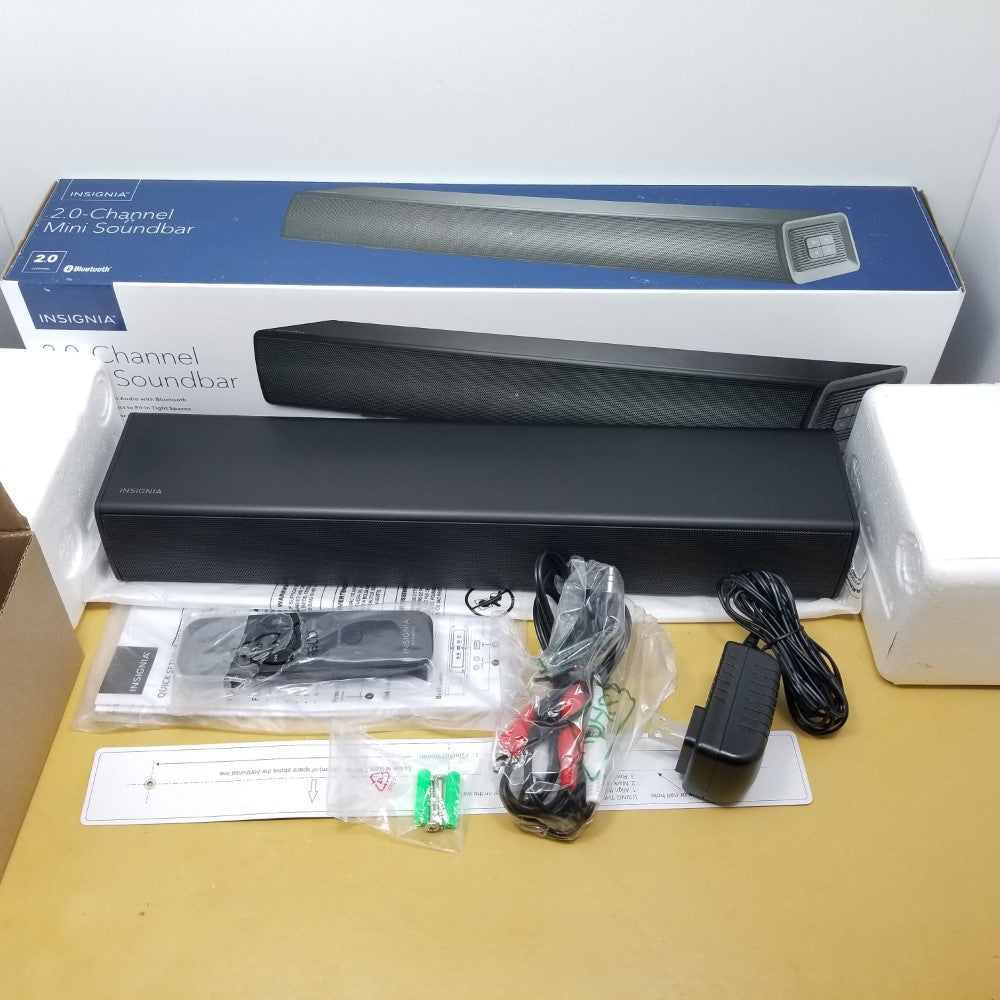 Insignia 2.0 channel mini soundbar with packaging and accessories on a table.