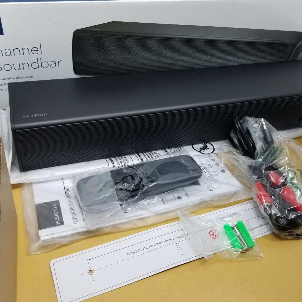 Soundbar with packaging, remote control, and cables on a yellow surface