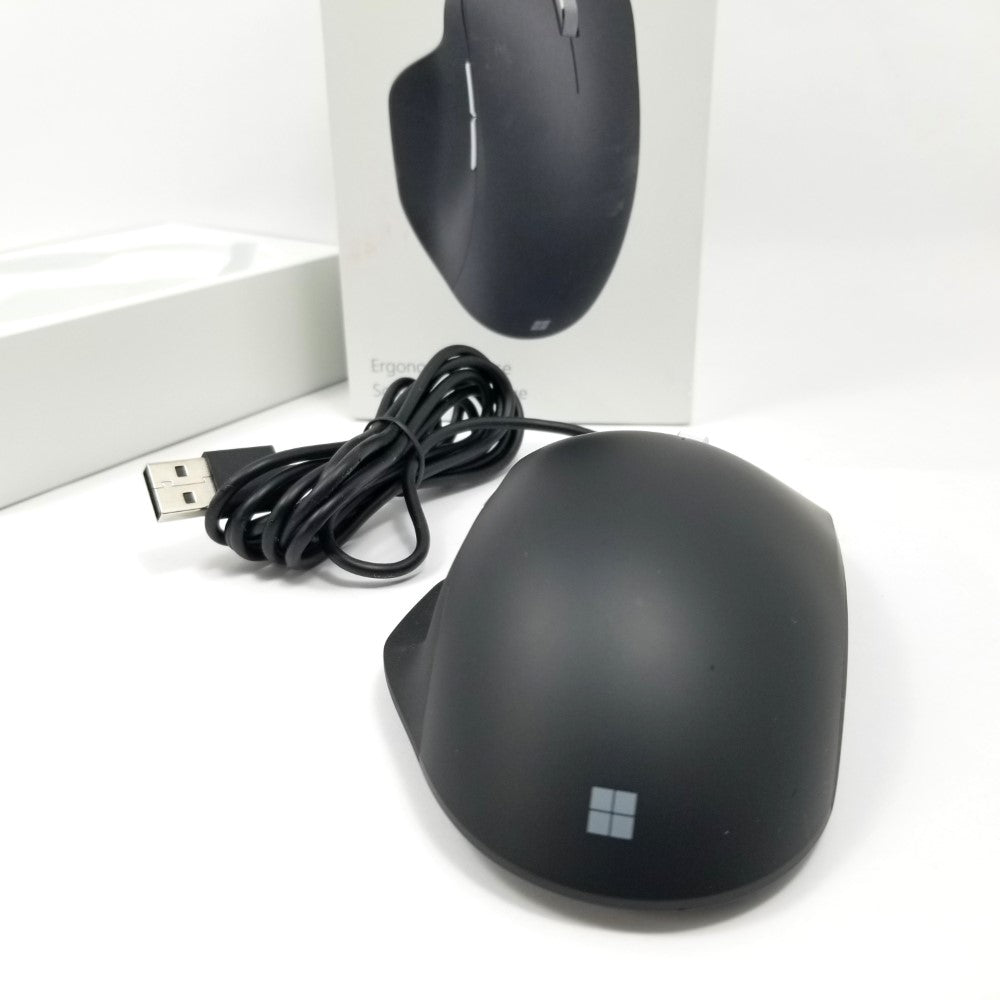Microsoft wired ergonomic mouse back side sitting on white surface with packaging in the background.
