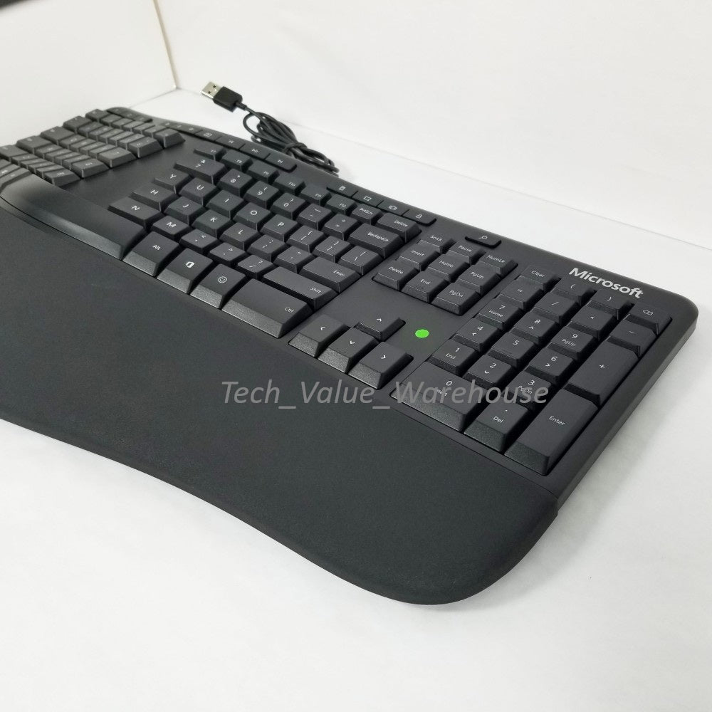 Side profile Microsoft ergonomic Keyboard with visible wire and USB plug, sitting on a white surface