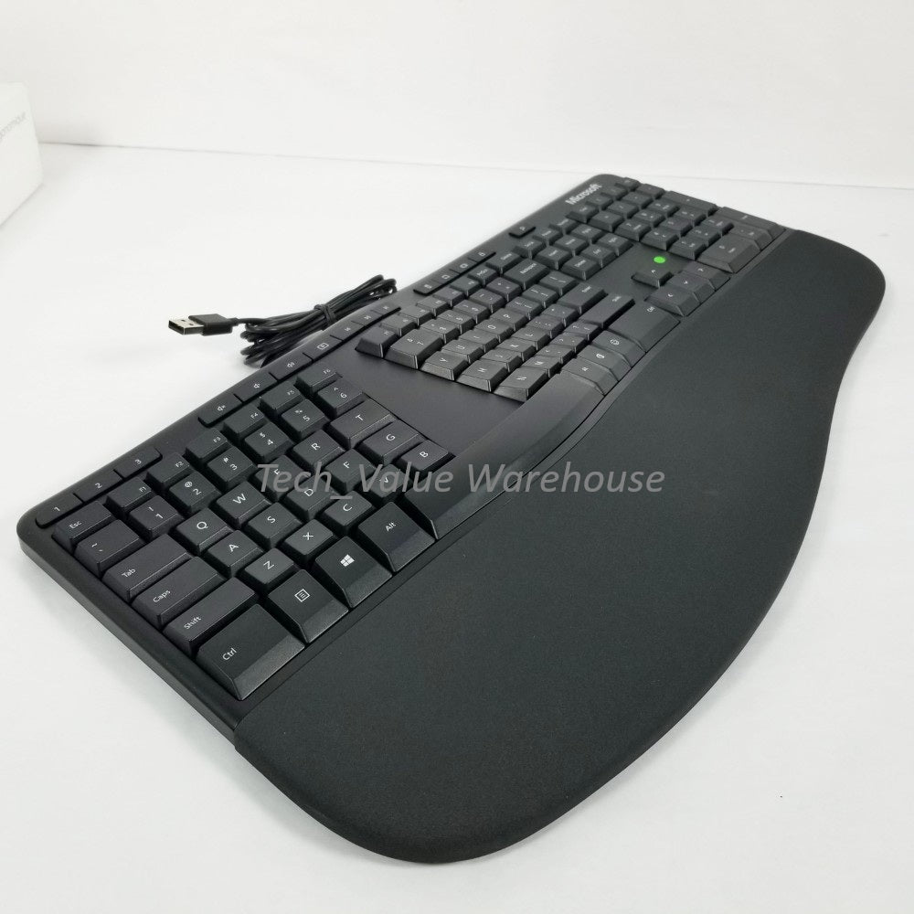 Side profile Microsoft ergonomic Keyboard showing palm rest, with visible wire and USB plug, sitting on a white surface.