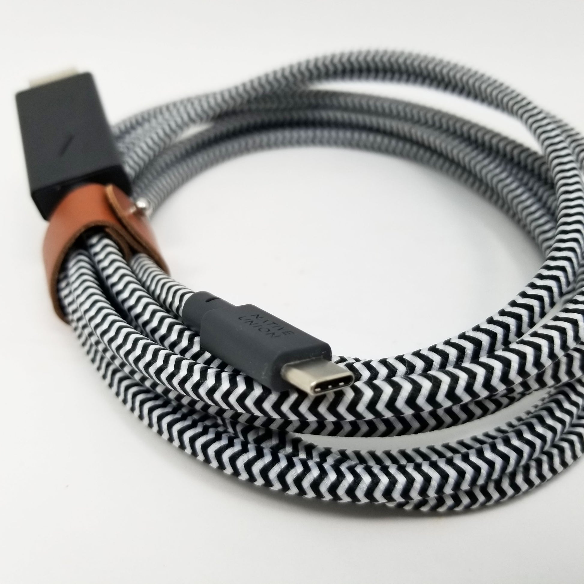 Native union coiled cable with zebra pattern tied with brown leather strap on a white background.