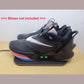 Black Nike Adapt shoes with two green lights on the side, sitting on Charging Mat on a beige surface. Also notation saying "shoes not included" can be seen next to shoes.
