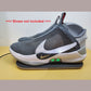 Gray Nike Adapt shoes with two green lights on the side, sitting on Charging Mat on a beige surface. Also notation saying "shoes not included" can be seen next to shoes.