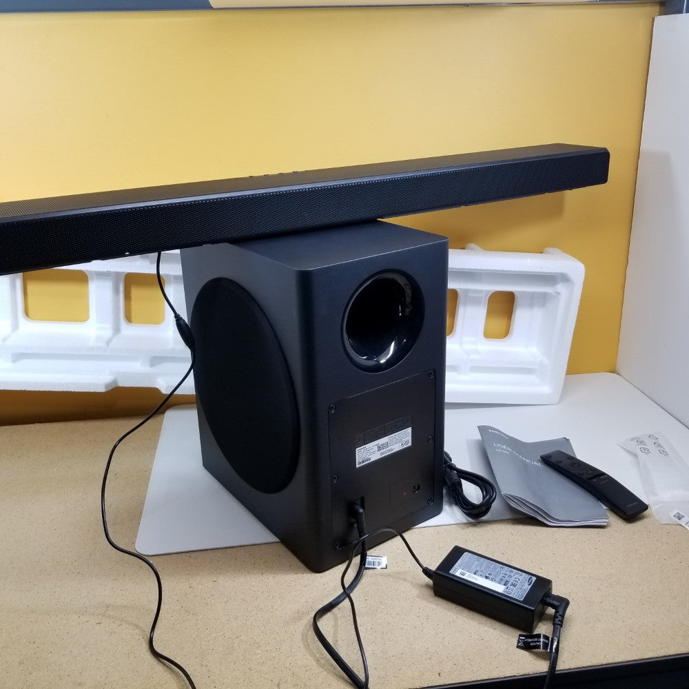 Black Samsung soundbar with subwoofer on a table with packaging materials in the background