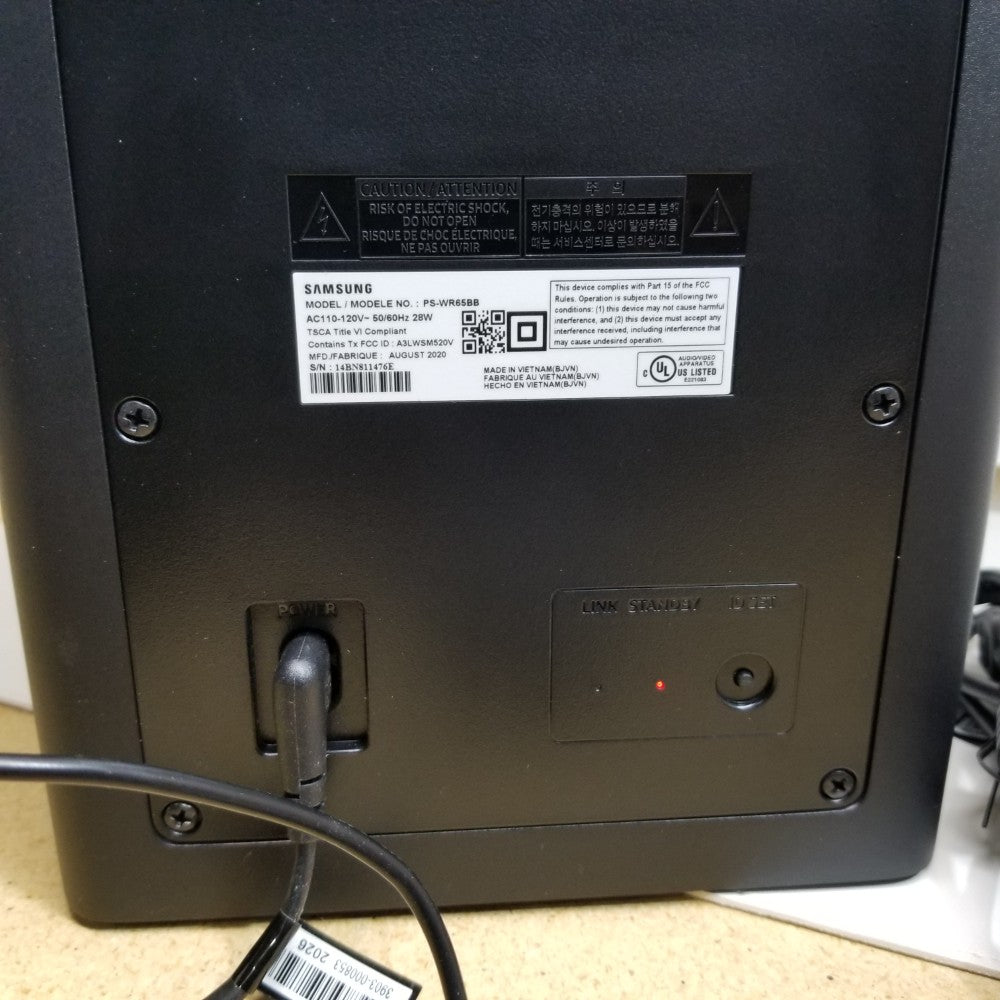 Back view of Samsung HW-Q60T subwoofer with labels and ports on a beige surface.