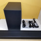 Samsung HW-Q60T subwoofer & soundbar with cables and power adapter on a white surface against a yellow wall.